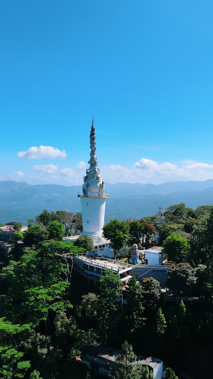 Distancing from a stunning Ambuluwawa Tower Temple in the suburbs of Gampola Town, Sri Lanka. Mountains silhouettes and blue skies at backdrop. Vertical video.