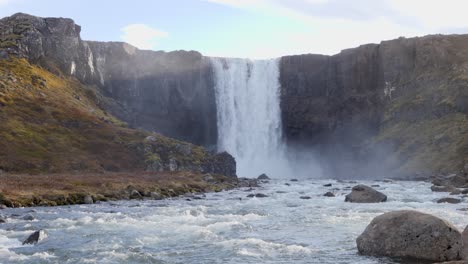 water falling down over a high waterfall seydisfjordur i niceland on a sunny day