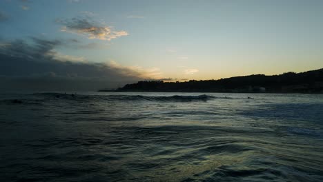 Aerial-drone-forward-view-over-surfers-having-fun-riding-waves-at-sunset