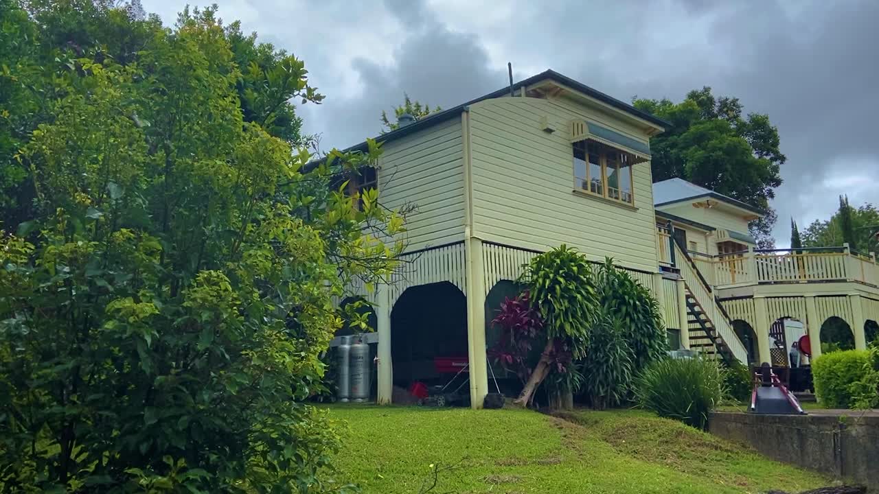 toma de revelación cinematográfica suave y lenta de la parte trasera de una casa de campo tradicional clásica de queensland, con una terraza trasera espléndida, enclavada en un jardín cuidadosamente cuidado