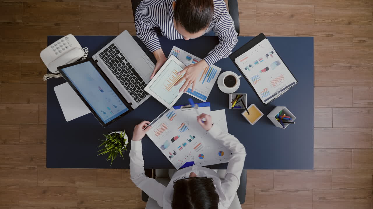 Top view of business women comparing financial graphs with management statistics expertise