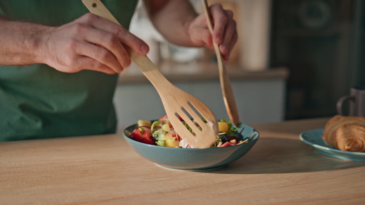 Man hands mixing salad at home kitchen closeup. Young guy preparing healthy food