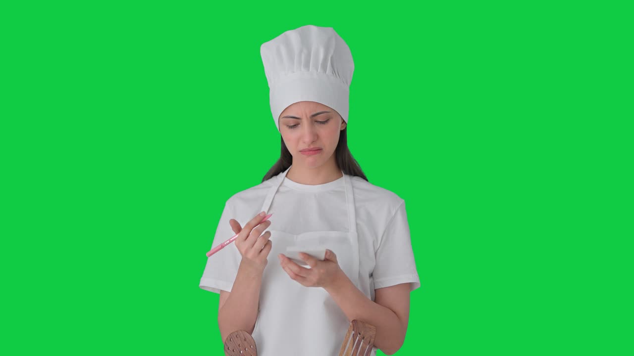Cuoca professionista indiana confusa che annota la ricetta, schermo verde