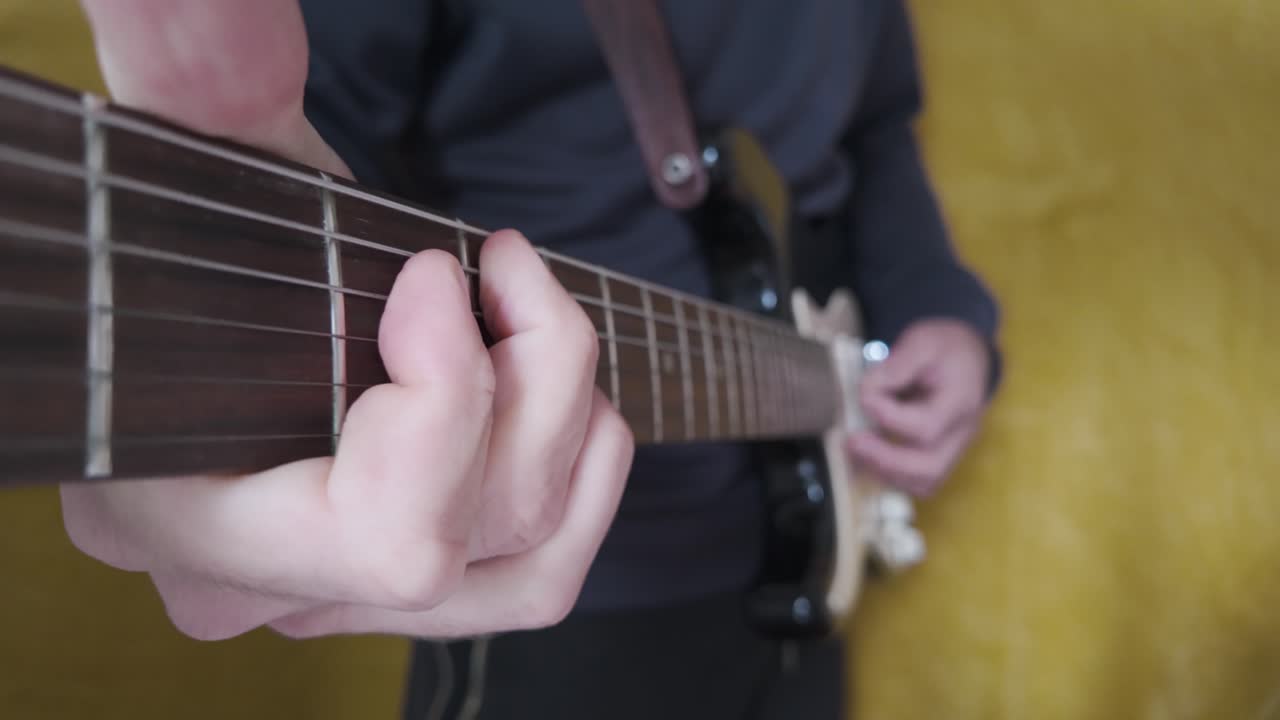 Close up view of a musician's hand skillfully playing electric guitar chords, capturing the vibrant essence of rock and pop music against a yellow background