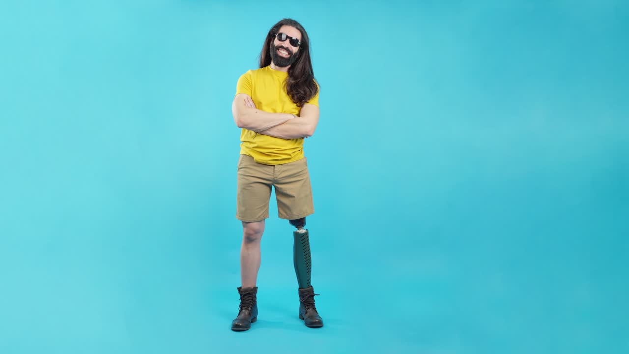 Man with prosthetic leg wearing sunglasses and yellow shirt standing on blue background