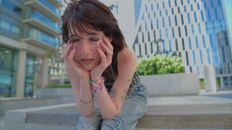 retrato de moda al aire libre de una mujer joven de estilo alternativo con tatuajes y perforaciones sentada fuera de edificios modernos filmada en tiempo real 2