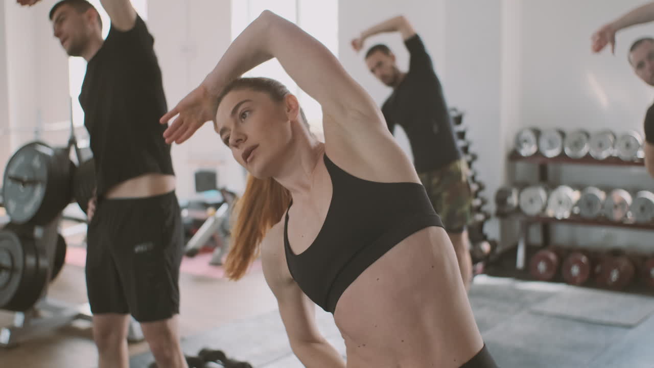 강하고 운동 능력이 뛰어난 젊은 여성이 일부 파트너와 함께 체육관에서 스트레칭 운동을 합니다.