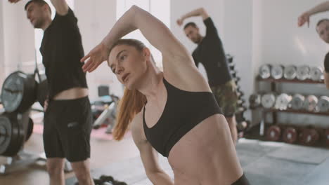 a strong and athletic young woman does stretching exercises in the gym with some partners