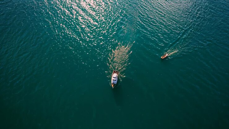 Drone che riprende un motoscafo di medie dimensioni che si allontana lasciando una scia attraverso la baia con una piccola barca che si dirige verso il largo