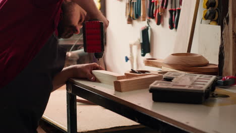 cabinetmaker drills hole into lumber block, doing furniture assembling