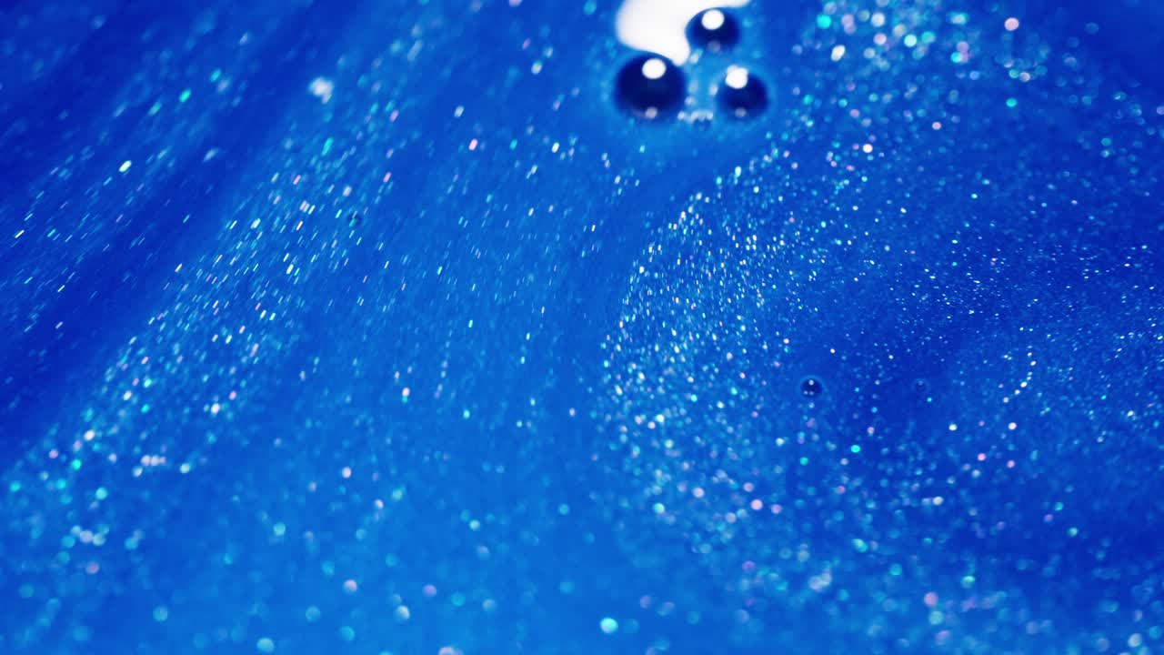 Mix of blue ink with glitter and bubbles in close-up shot, showcasing fluid dynamics