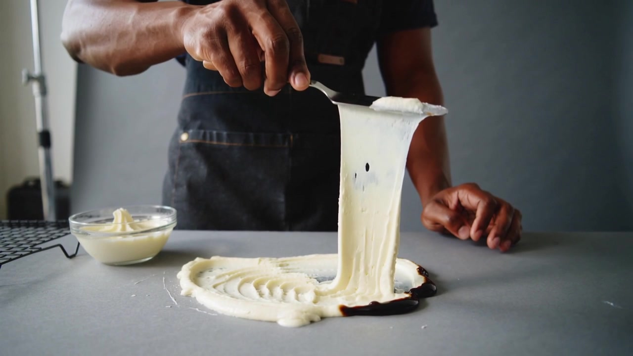 After smoothing chef dark apron lifting offset spatula pulling cream into ribbon testing in kitchen