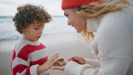 smiling mom teaching kid at seaside closeup. cute little boy counting stones