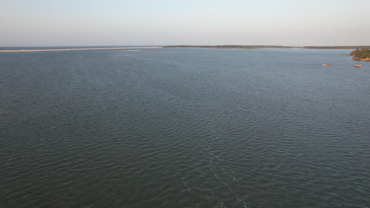 Drone flying over Preguiça river, in Maranhao, Brazil. A boat and a kitesurf. Soft light of the sunset. Some houses on the beach.