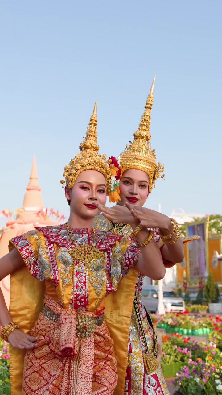 Duas performers femininas com trajes dourados ornamentados dançam graciosamente ao ar livre durante o dia claro