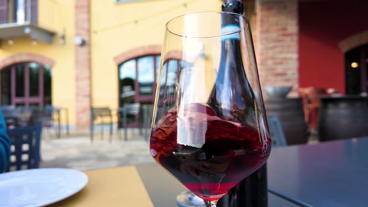 Primo piano di vino rosso che volteggia in un bicchiere su una terrazza soleggiata di un ristorante piemontese.