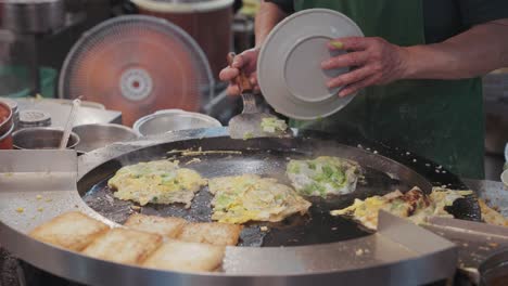 street vendor frying and flipping sizzling taiwanese oyster omelette on a hot round griddle, with eggs, oysters, and batter bubbling together into a savory street food delicacy