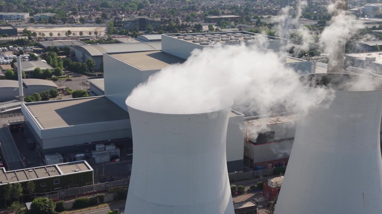 Vista aerea di una centrale elettrica multi-combustibile di giorno. Le torri di raffreddamento rilasciano grandi pennacchi di vapore. Questo impianto di termovalorizzazione genera energia da vari combustibili.