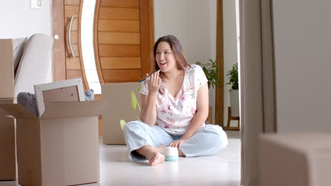 happy plus size biracial woman talking on phone on floor of new home, copy space, slow motion