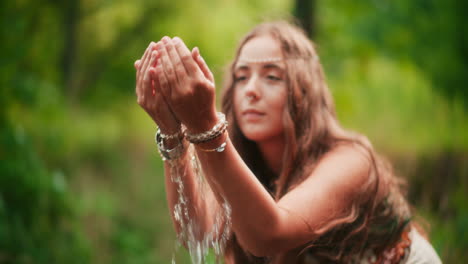 una mujer toma agua de montaña cristalina en sus manos