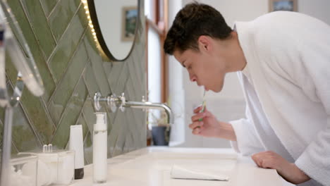 biracial man brushing teeth in morning in bathroom, copy space, slow motion