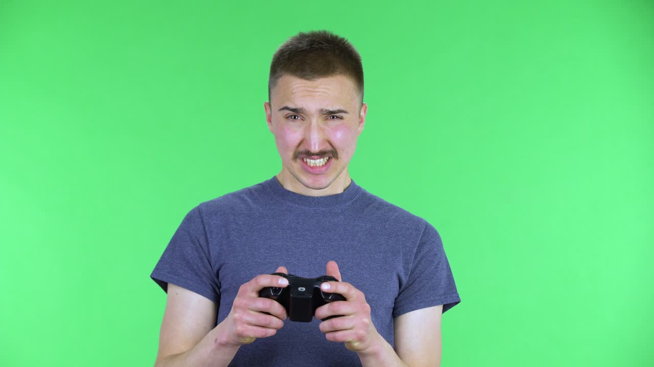 retrato de un joven jugando a un videojuego usando un controlador inalámbrico regocijándose en la victoria y se molesta por perder. lindo hombre con bigote posando en una pantalla verde en el estudio. cerca