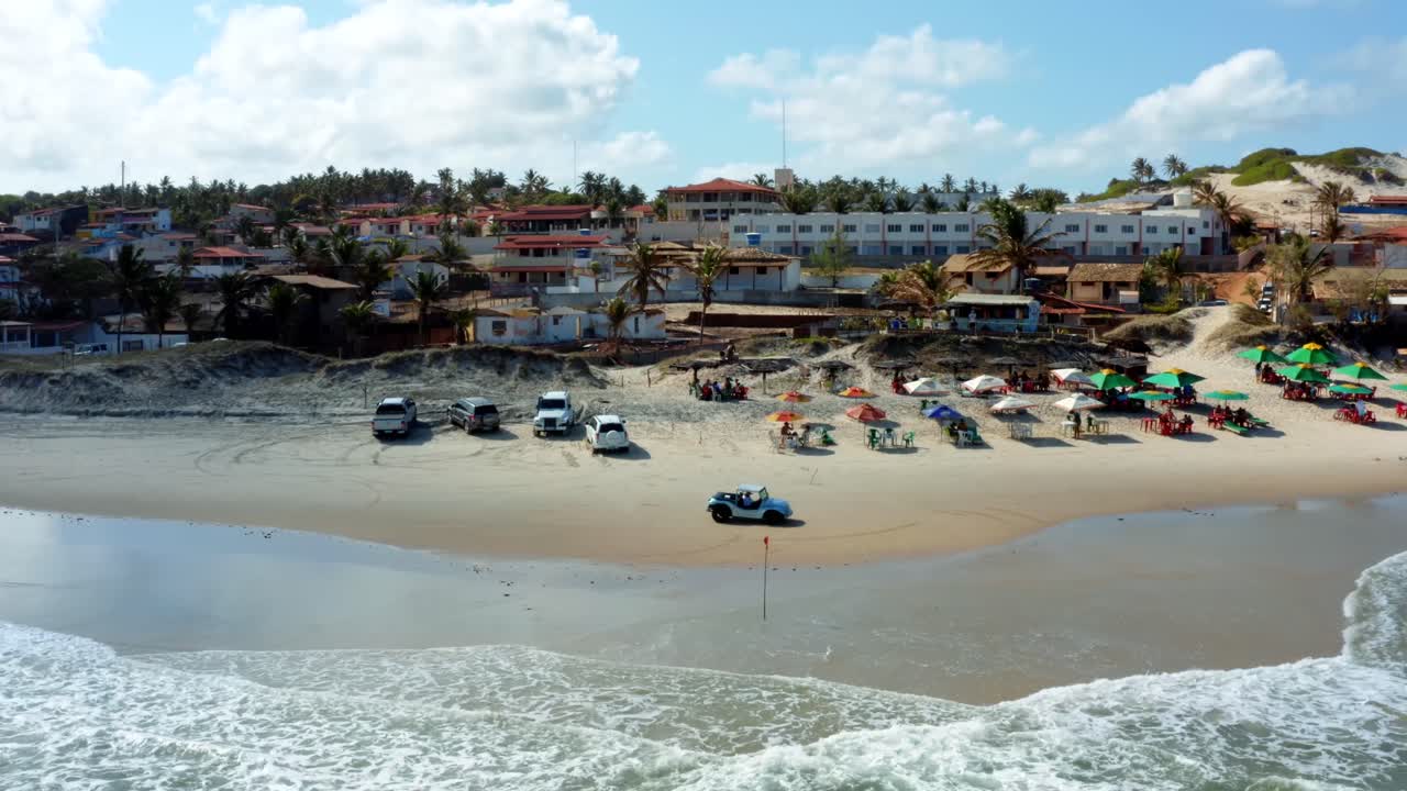 toma aérea con drones de una hermosa playa tropical en sibauma cerca de pipa en el norte de brasil con sombrillas turísticas, arena dorada, agua clara, buggies de arena y casas de playa