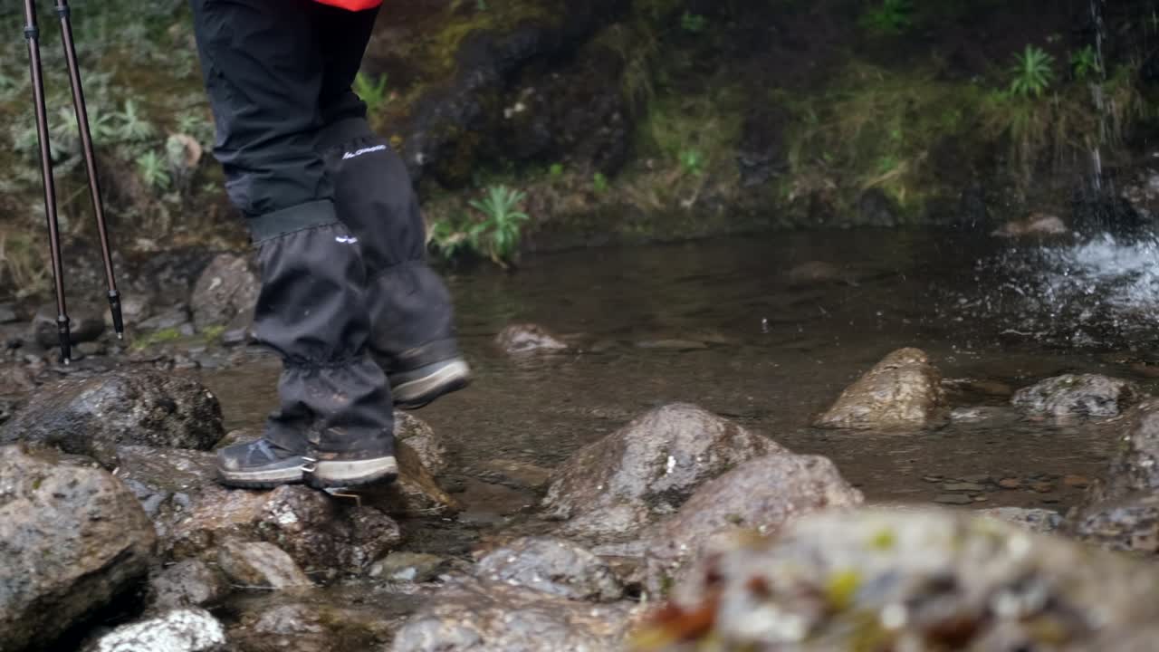 Close-up of the legs of a female hiker walking on rocks past a waterfall