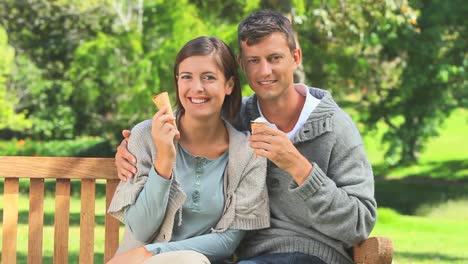 una joven pareja comiendo helado mientras está sentada en un banco