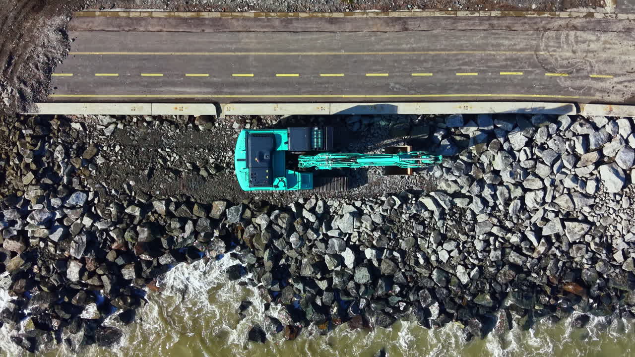 Un mezzo da costruzione opera su una costa rocciosa vicino all'acqua durante il giorno, mentre prepara la strada e il litorale per il completamento del progetto.