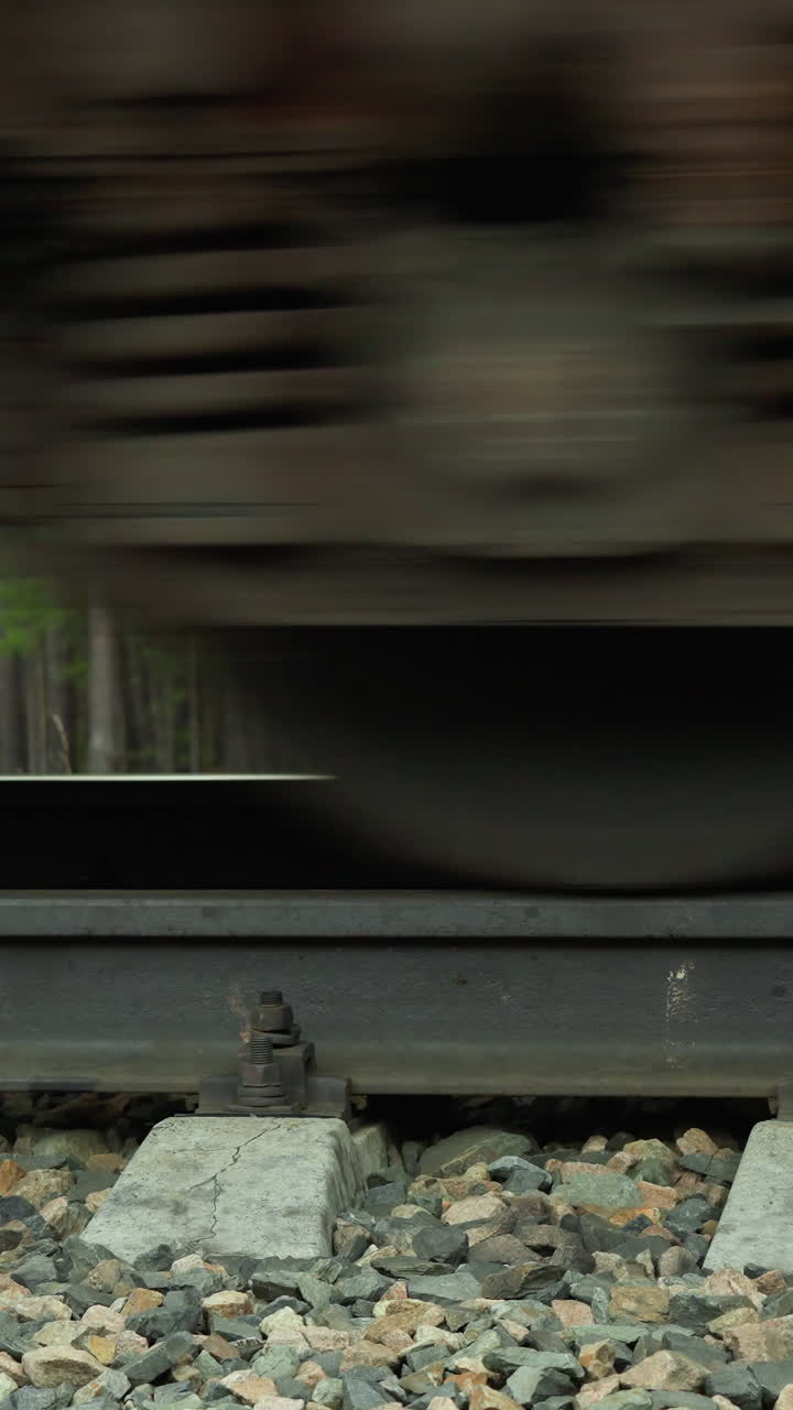 철도 트랙을 지나가는 열차 바의 근접 뷰, 바의 모션 흐릿함은 속도와 움직임을 전달하고, 트랙과 자갈 침대는 숲의 배경으로 명확하게 볼 수 있습니다.