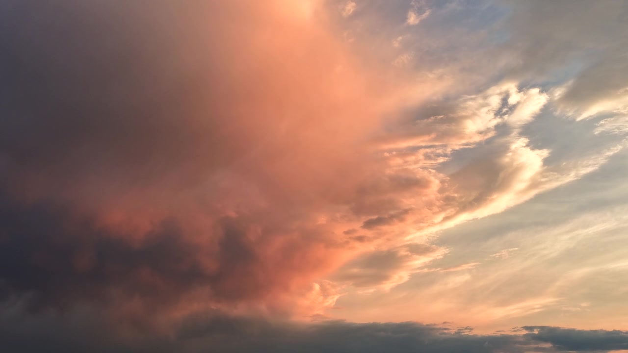 4K UHD drone timelapse of a dark rain system mixing with heavy wildfire smoke. The dense cloud mass glows with an eerie orange and pink hue against the blue sky, highlighting extreme weather.