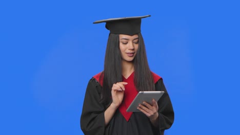 retrato de una estudiante en traje de graduación de gorra y túnica, viendo información en una tableta digital. mujer joven posando en el estudio con fondo de pantalla azul. primer plano. cámara lenta lista 59.94fps