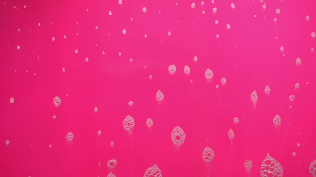 Foam bubbles from soap flowing on pink background.