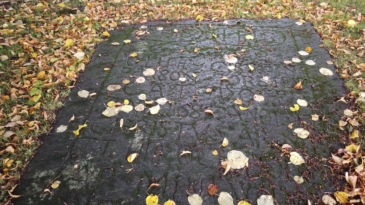 Ancient flat tombstone on leafy autumn ground in Sweden, slow tilt up