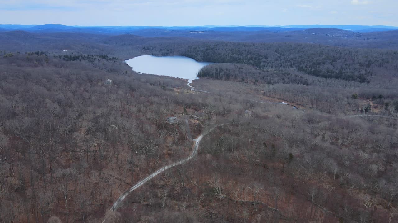 Aerial drone footage of vast wilderness with bare tree canopy and a lake in the distance during winter in the Appalachian Mountains