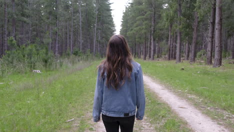Girl-walking-along-trail-amongst-tall-green-trees-in-a-forrest