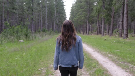 girl walking along trail amongst tall green trees in a forrest