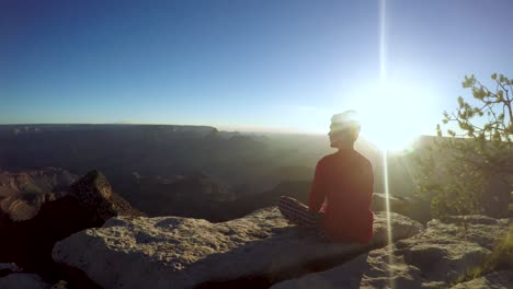 young man sits on the edge of a huge canyon at sunrise