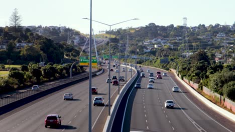una amplia toma de mano de la autopista de auckland siendo atravesada por varios vehículos que se mueven a alta velocidad en una tarde soleada, con un vecindario en el fondo en la ciudad de auckland, nueva zelanda