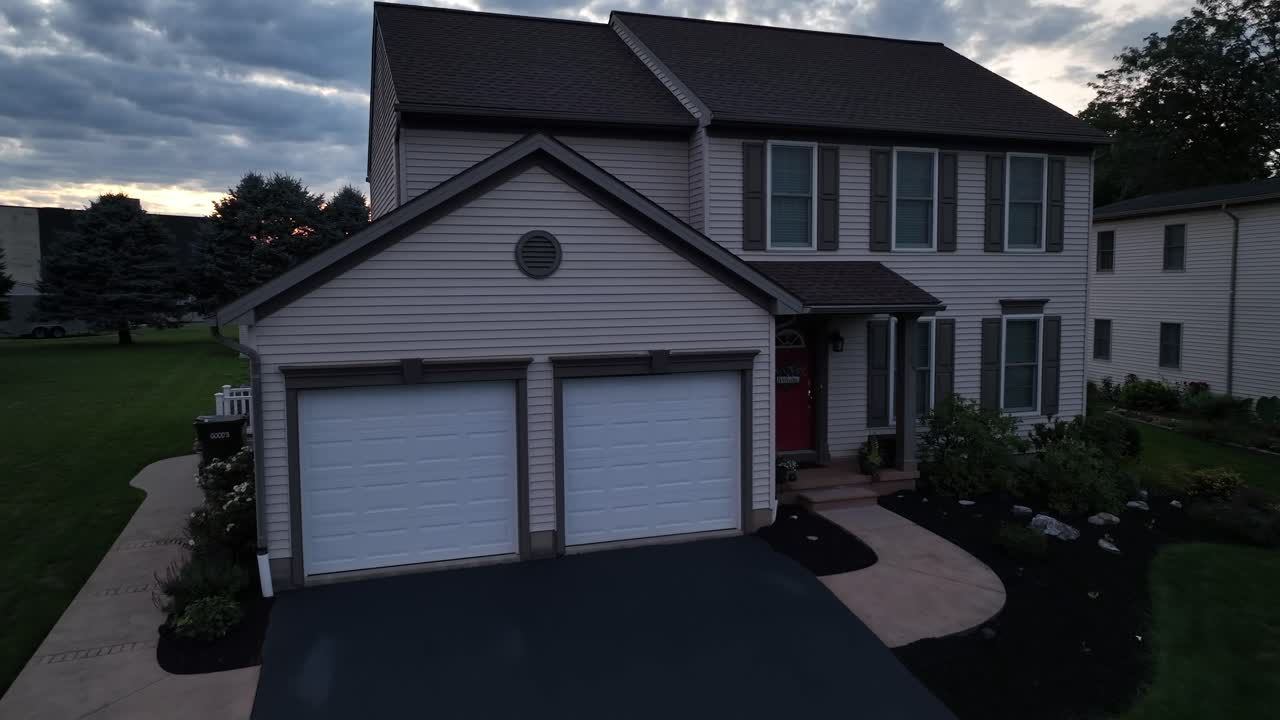 American single family house with double garage after sunset time. Green grassy garden with driveway in american neighborhood. Aerial approaching shot.