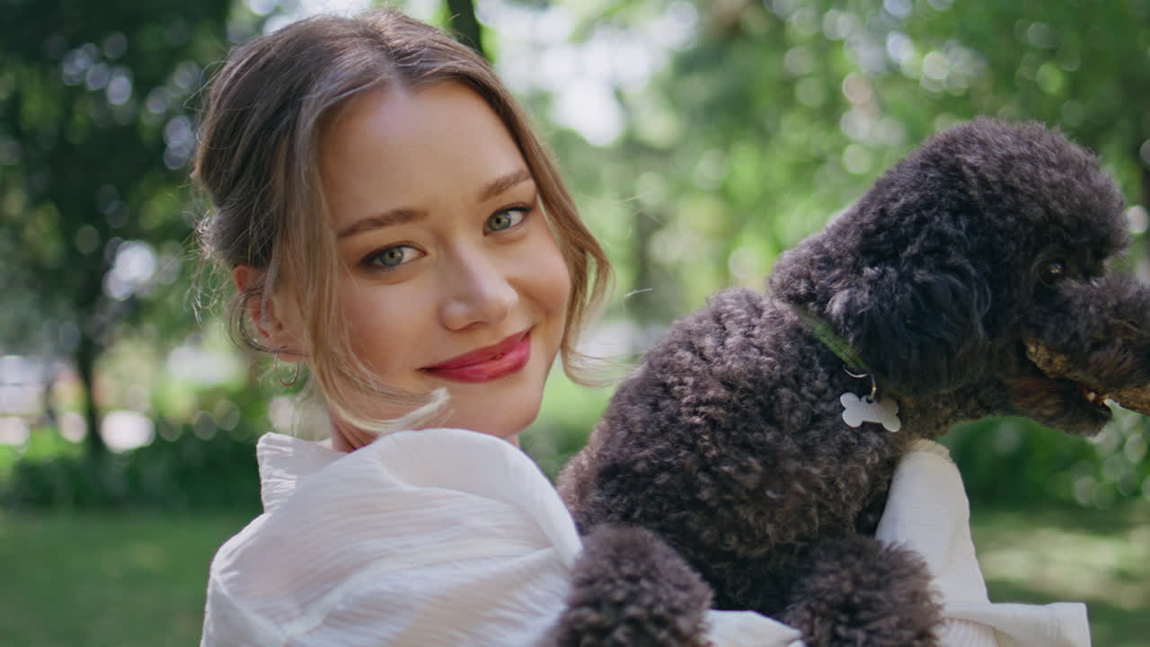 Smiling woman holding poodle on sunny nature closeup. Joyful girl cuddling dog