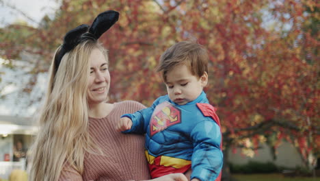 Mama-Trägt-Ein-Baby-In-Einem-Superheldenkostüm-Auf-Dem-Arm,-Sie-Gehen-An-Halloween-Süßigkeiten-Essen