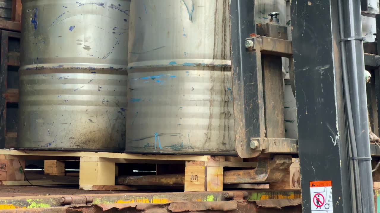 Un operario industrial conduce una carretilla elevadora para transportar barriles de acero en la zona de almacenamiento de una fábrica. Concepto de logística de almacén y manipulación de materiales