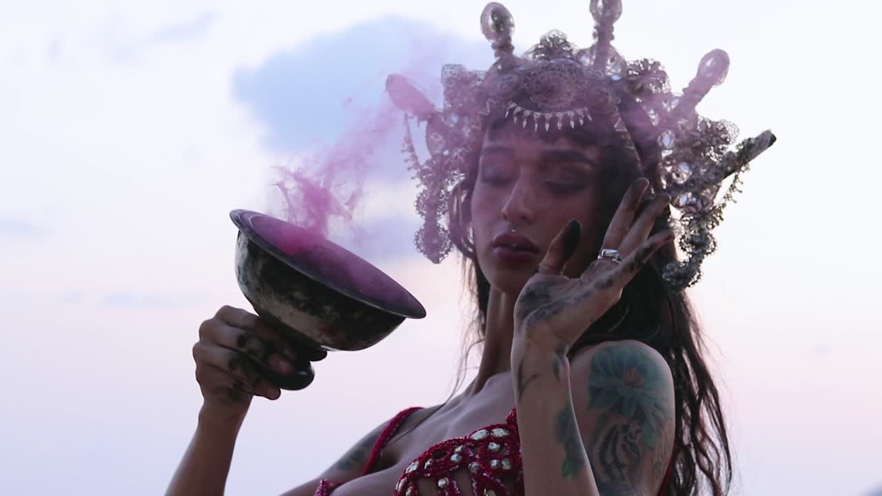 Close up of young and sexy belly dancer performing figure 8 move with pink color smoke bomb, on the beach. Slow motion