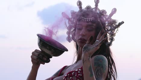 close up of young and sexy belly dancer performing figure 8 move with pink color smoke bomb, on the beach. slow motion