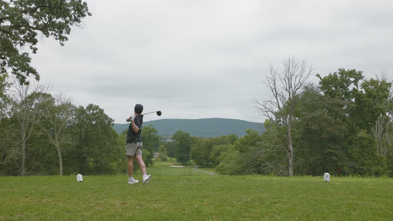 Golfer swings a driver off the tee box on a lush golf course, ideal for sports, recreation, and outdoor activity visuals