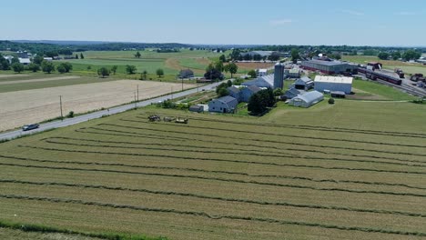 Eine-Luftaufnahme-Eines-Amish-Bauern-Mit-Fünf-Pferden,-Der-Seine-Ernte-Erntet-Und-Sie-An-Einem-Schönen-Tag-Auf-Einen-Karren-Lädt,-Der-über-Die-Landschaft-Blickt