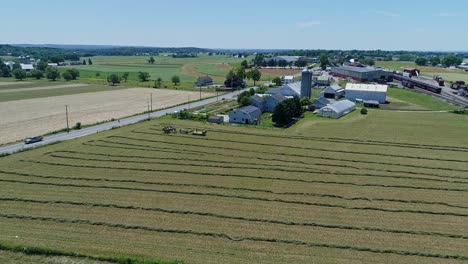 an aerial view of an amish farmers with five horses harvesting his crops and loading them on to a cart looking over the countryside on a beautiful day