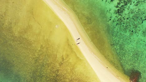 Tourists-on-narrow-stripe-with-white-sand-washed-on-both-sides-by-colorful-shallow-lagoon-with-coral-reefs,-sea-texture-in-Caribbean